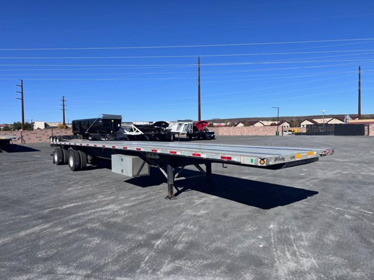 Flatbed trailer in an open lot showing long aluminum deck and dual rear axles with a gooseneck hitch area.