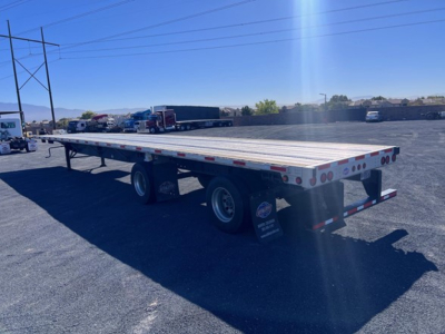 Flatbed trailer in a yard showing dual rear axles and reflective tape along the sides, 2024 Utility 4000Ae listed as used.