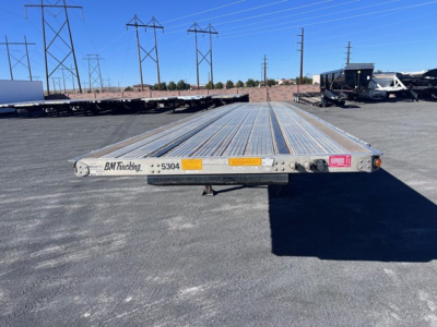 Flatbed trailer by BM Trailers showing long low-profile deck with multiple crossmembers and rear bumper label, 2024 Utility 4000Ae listing context in background.
