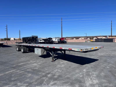 Flatbed trailer in an open lot showing long aluminum deck and dual rear axles with a gooseneck hitch area.