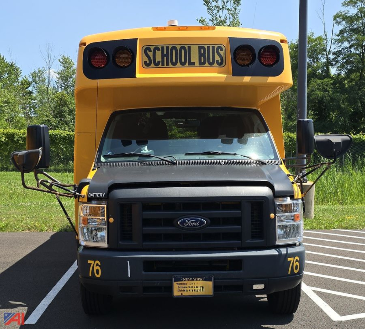 Front view of a 2018 Ford EC4 micro bus with wheelchair lift, yellow school bus with black grille, 'SCHOOL BUS' sign on top, front bumper numbers 76, mirrors extended.
