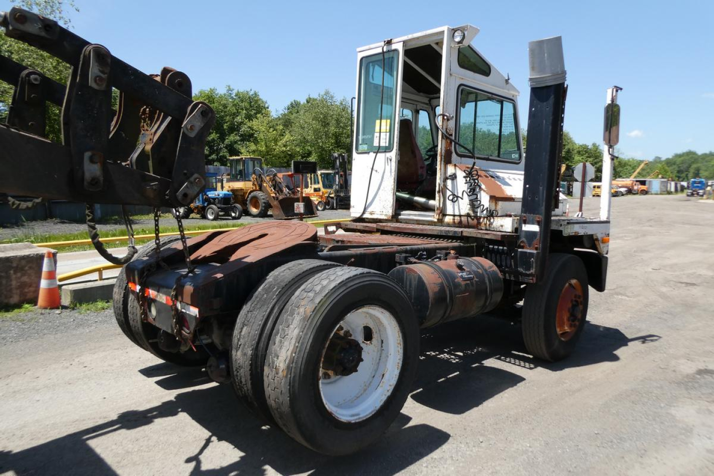 Truck tractor in yard showing chassis and cab with dual rear wheels and a heavy front hitch attachment.