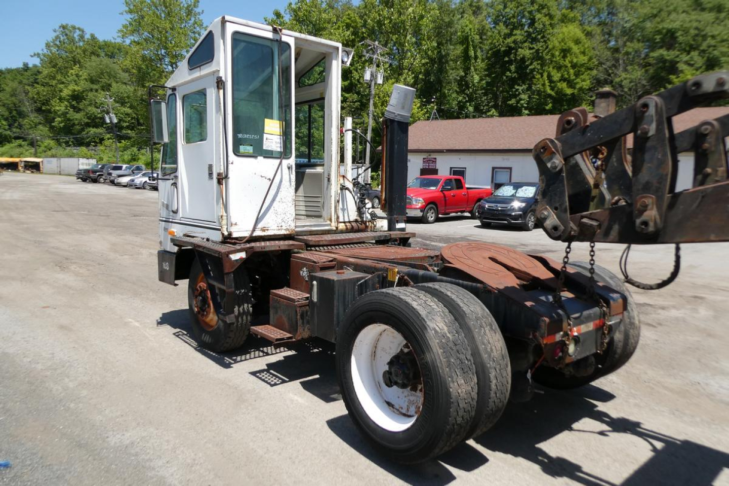 Truck cab and chassis of a 1999 Ottawa yard truck viewed from the side, showing a white cab with a crane arm and black chassis.