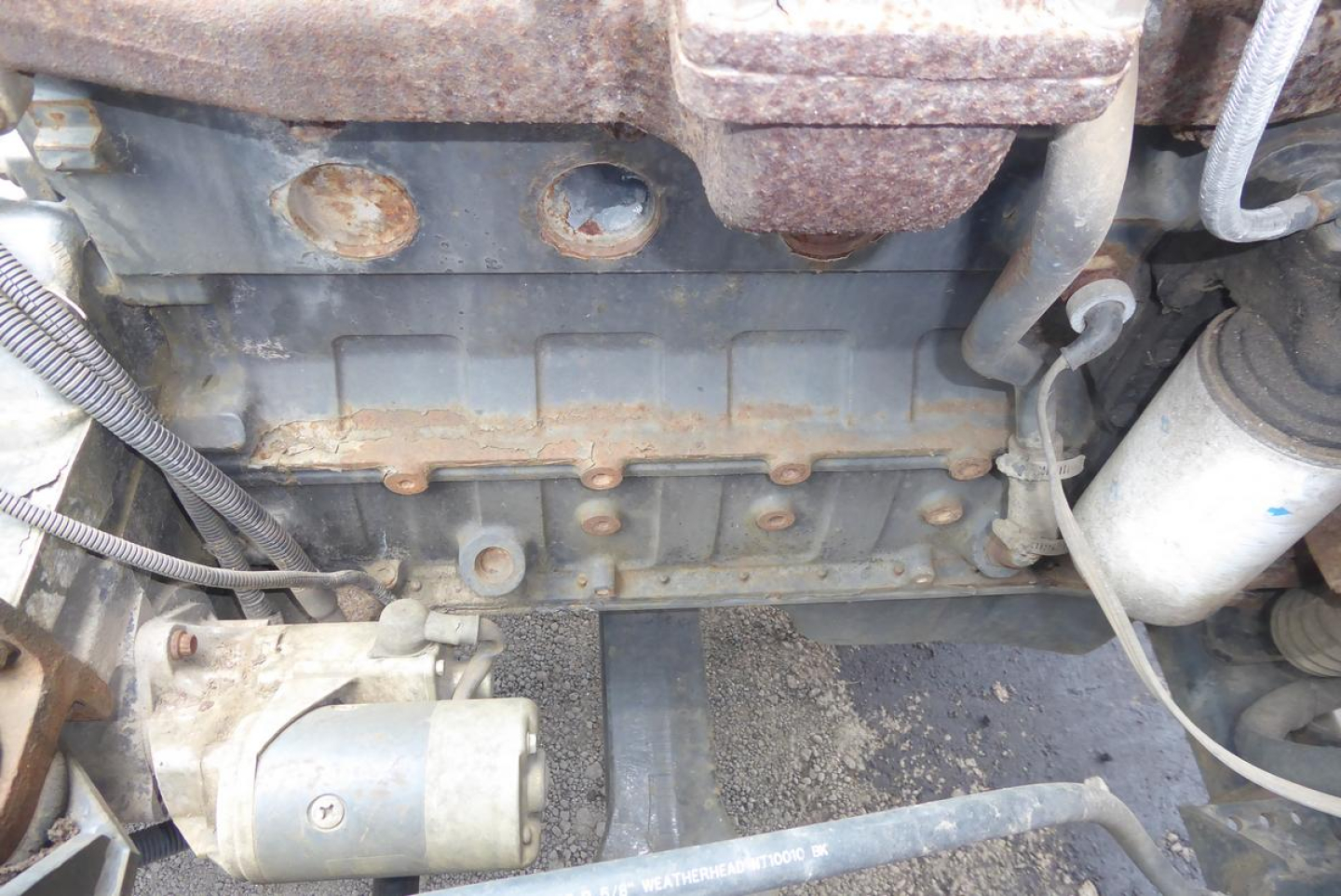 Engine bay of a used Ottawa 30 truck showing engine block with visible bolts, hoses, and a battery/alternator area.