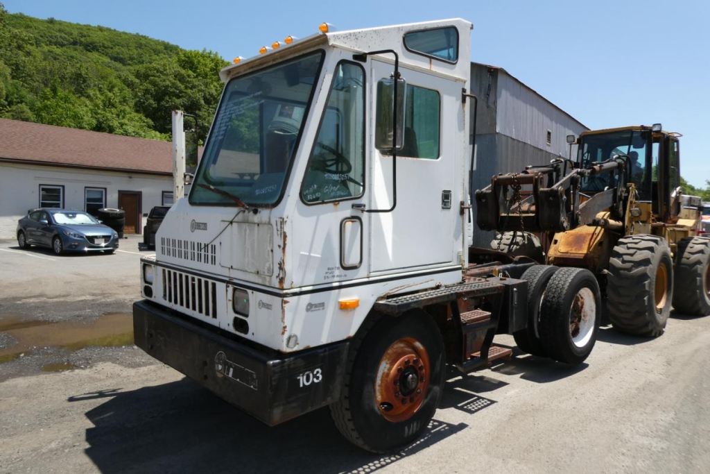 Truck tractor cab in front view with Ottawa branding and attached heavy equipment on the back, white cab, orange wheel rims, side mirrors, and multiple orange lights on roof.