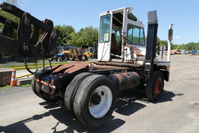 Truck tractor in yard showing chassis and cab with dual rear wheels and a heavy front hitch attachment.