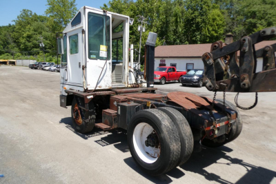 Truck cab and chassis of a 1999 Ottawa yard truck viewed from the side, showing a white cab with a crane arm and black chassis.