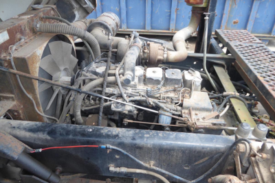Truck engine bay showing diesel engine with exposed components, radiator fan, hoses, and exhaust pipe in a yard truck.