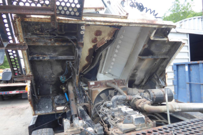 Truck engine bay showing exposed components and transmission between metal panels in a yard setting.
