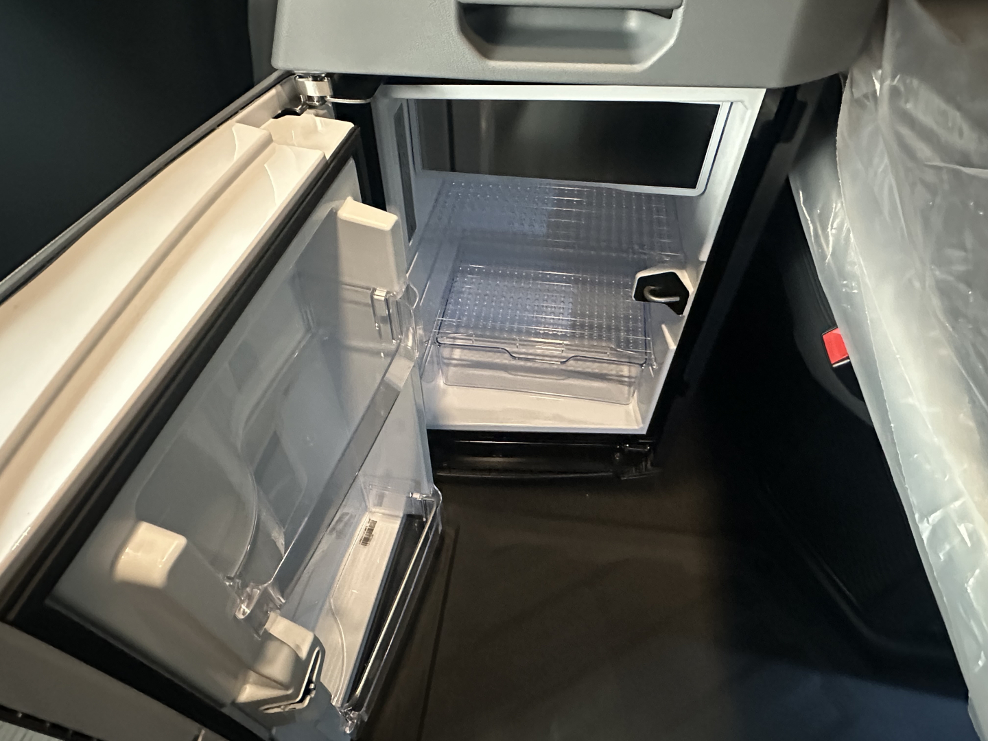 Interior view of a small refrigerator/freezer unit inside a Mack PR64T76H truck cab showing an open freezer compartment with a small refrigerator below.