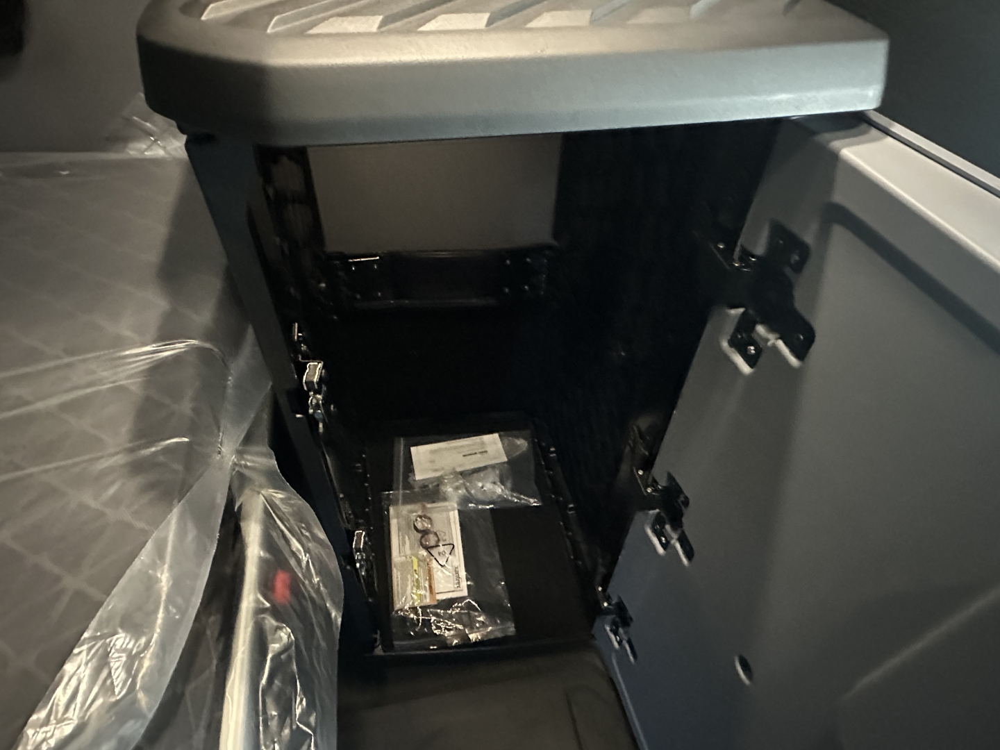 Cab interior of a new Mack PR64T76H sleeper cab showing an open storage compartment with a packaged item inside.