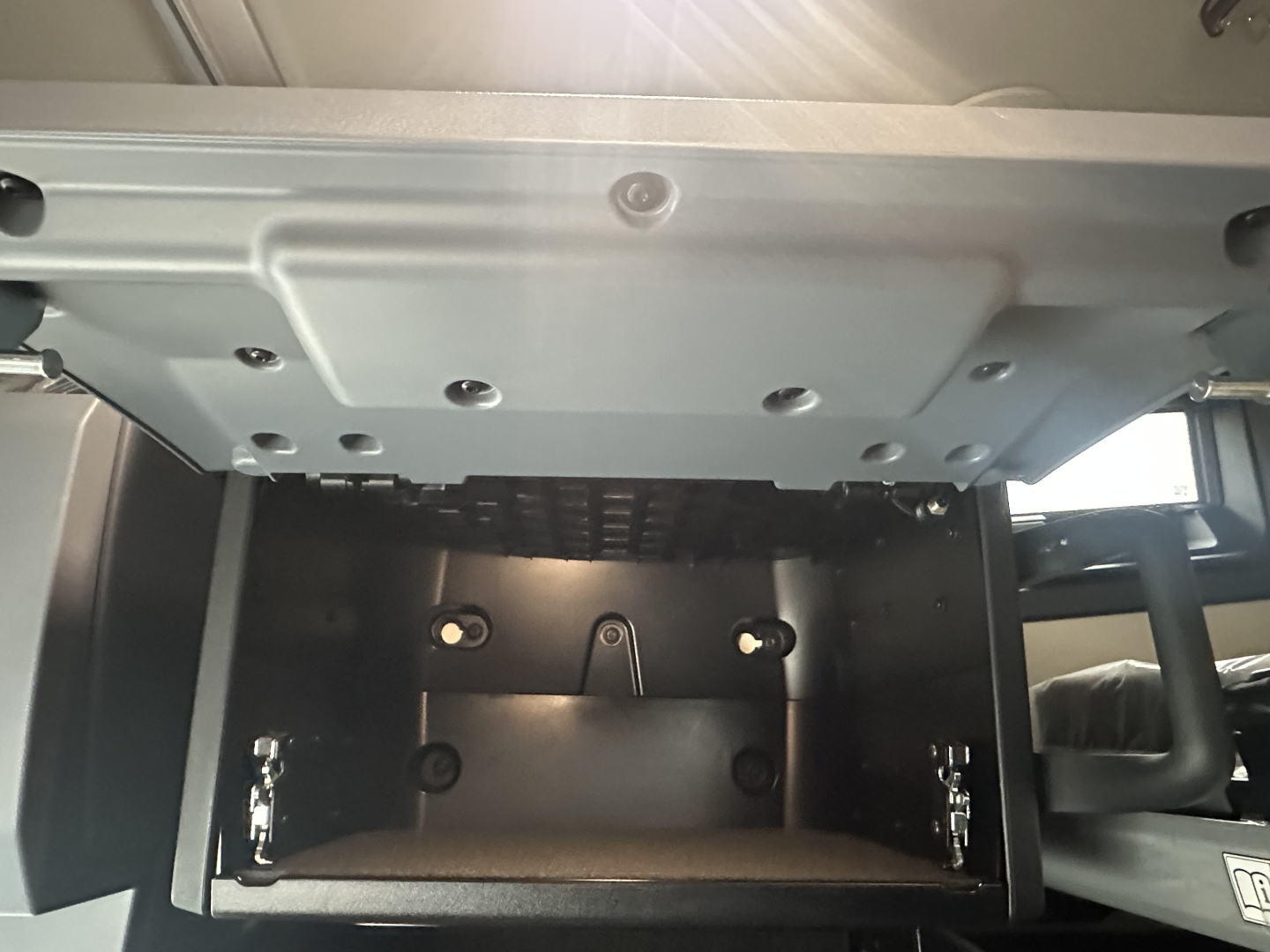 Truck cab interior dash area showing under-bunk storage compartment with black metal interior and latches.