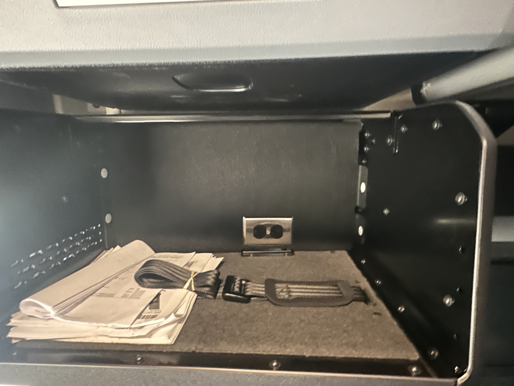 Truck cab storage compartment with manuals and a two-pedal scanner in a Mack PR64T76H engine bay area.