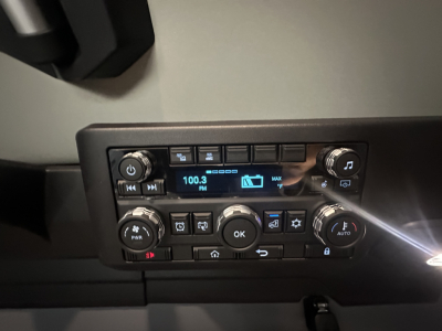 Cab dash cluster showing radio display 100.3 FM and multiple control knobs for climate and audio.
