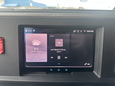 Truck cab interior touchscreen display showing weather and radio app, with dashboard bezel around.