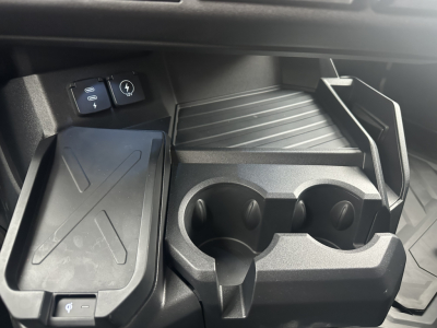 Interior center console of a new Mack PR64T76H truck showing cup holders and storage tray; visible control panel and USB-style port near dashboard.