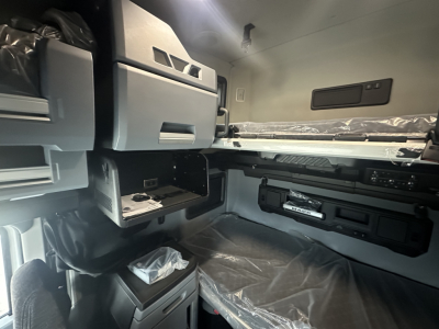 Cab interior of a Mack PR64T76H tractor sleeper showing overhead storage, dashboard consoles, and sleeping bunk with plastic covers.