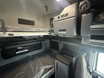 Truck sleeper cab interior showing overhead bunk with cabinets and storage, dashboard area, and window; no legible small print visible.