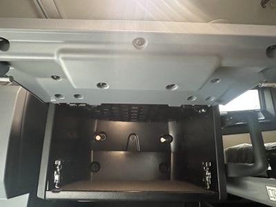 Truck cab interior dash area showing under-bunk storage compartment with black metal interior and latches.