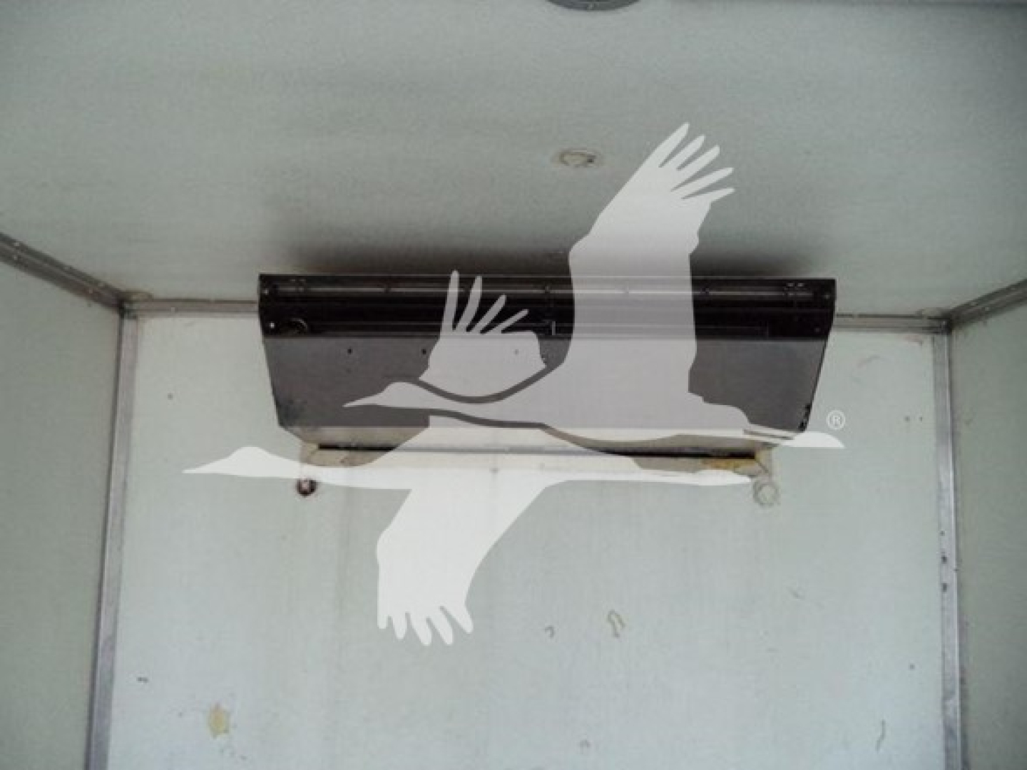 Refrigerated truck interior showing ceiling-mounted HVAC unit/back panel and a faint logo of a bird overlaying the image.