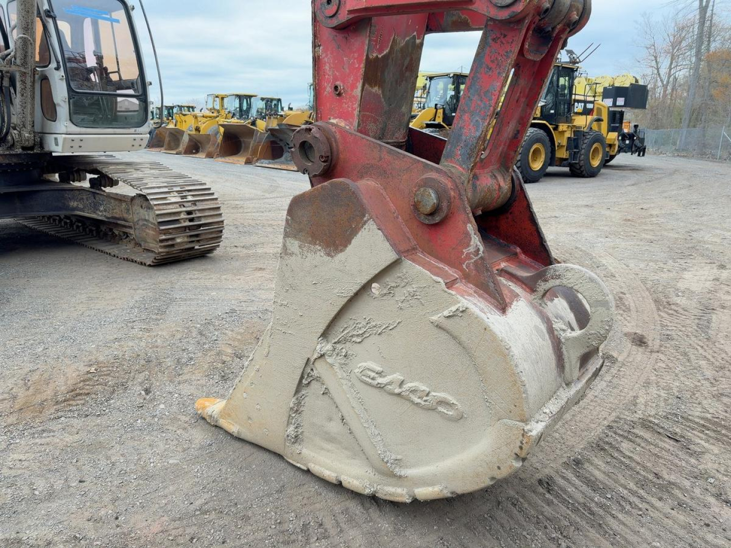 Excavator bucket attachment with Link-Belt logo and hydraulic arm in a yard showing other equipment in background.