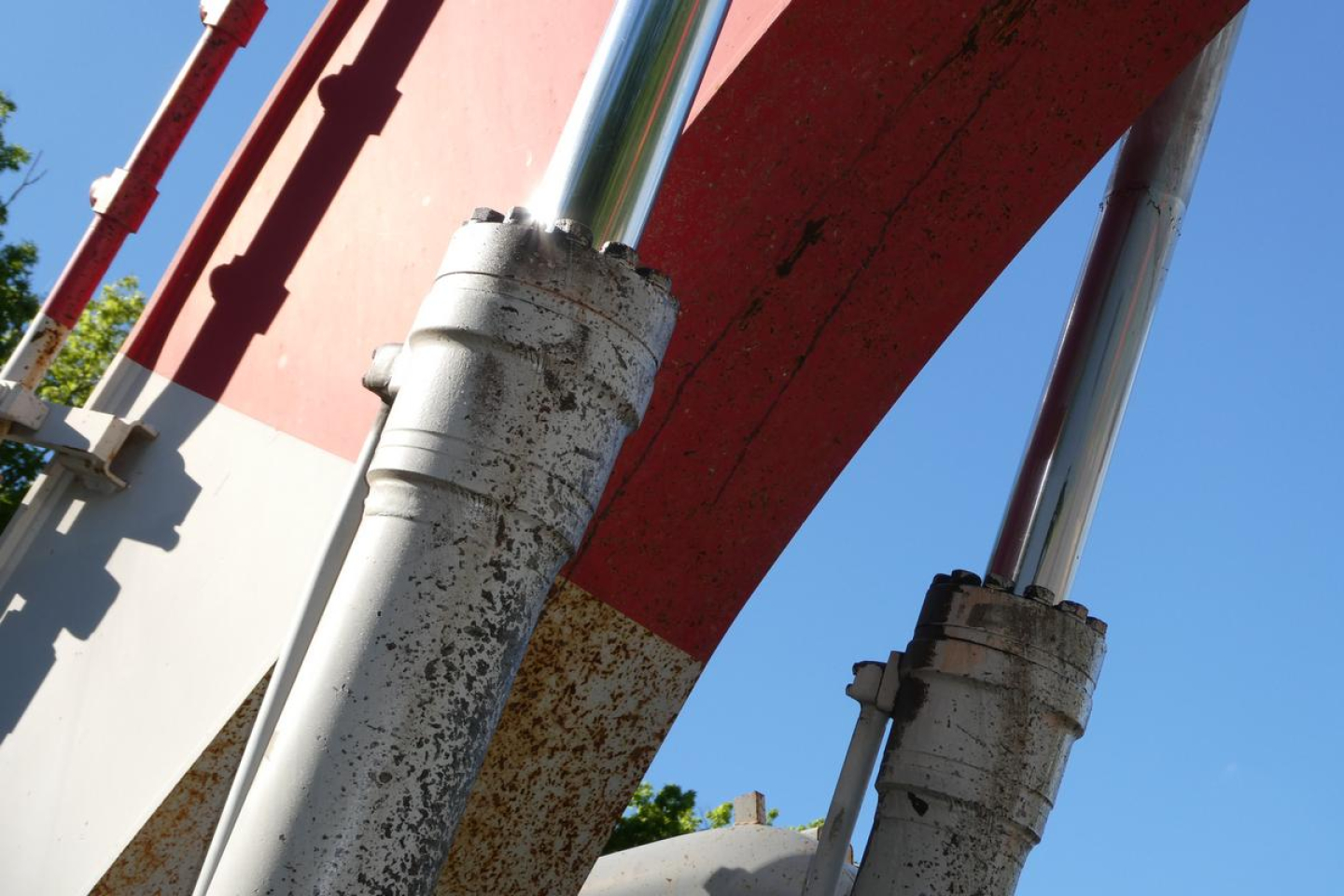 Excavator equipment showing hydraulic cylinder rods with weathered bushings and red structural beam.