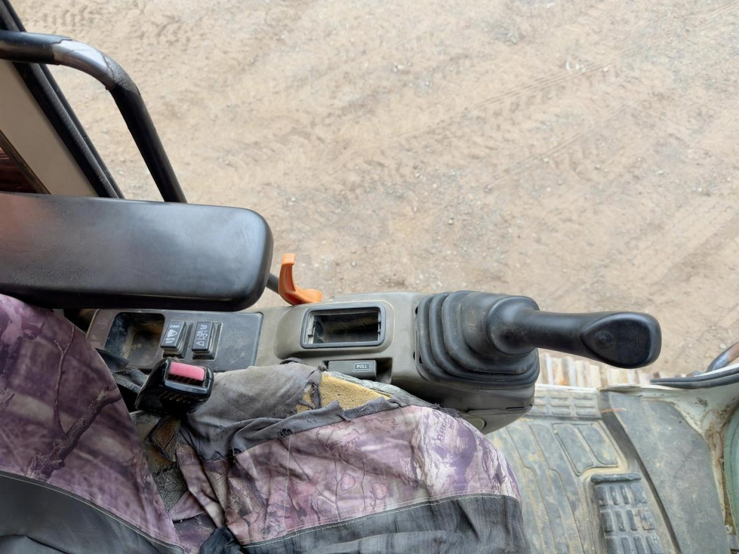 Operator cab interior of excavator showing joystick and controls; visible wear and cable boot, seat area, and control levers.