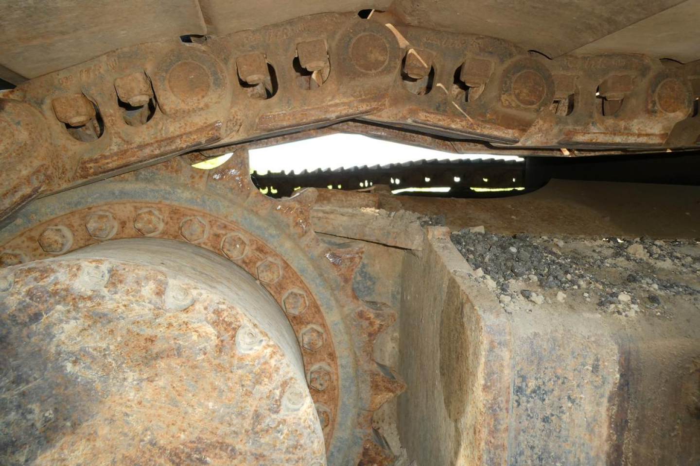 Sightline of a Link Belt excavator track assembly showing rust and metal rollers and the track chain links.