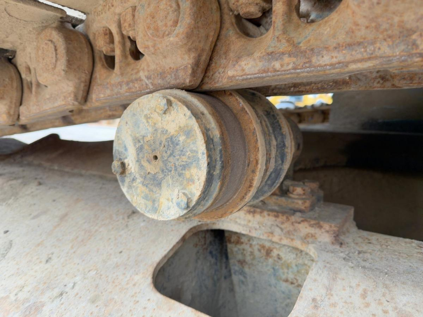 Excavator undercarriage wheel roller and track links with rust and dirt visible.