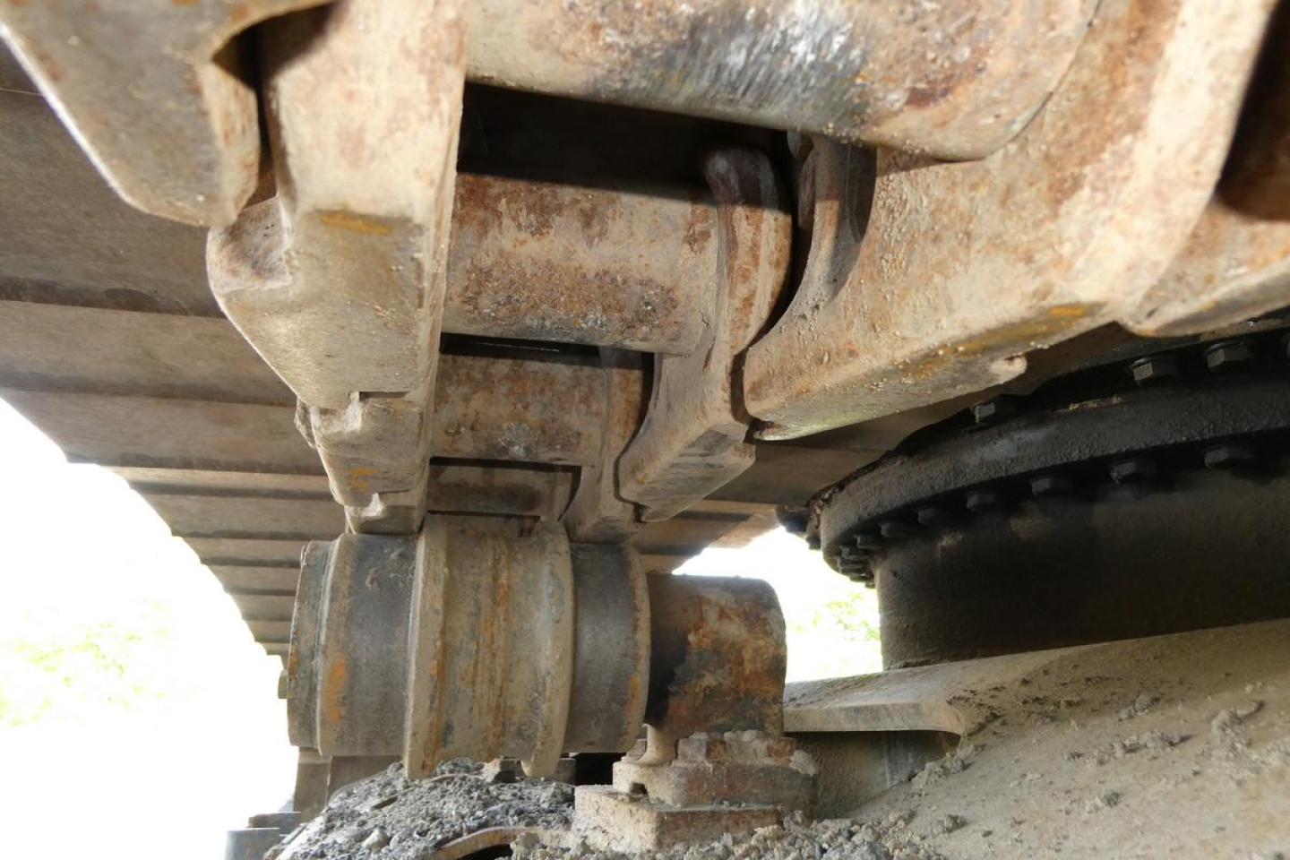 Link Belt 330LX excavator undercarriage showing track roller and sprocket with rust-colored metal and dirt buildup.