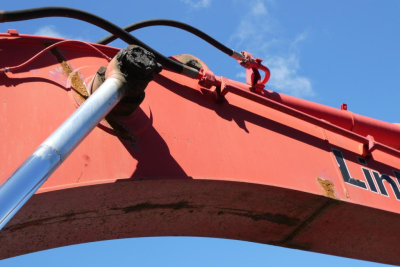 Excavator boom segment showing hydraulic hose and pin area with Link-Belt branding on red paint.