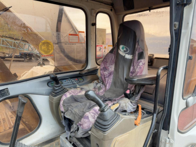 Excavator cab interior showing operator seat and two joysticks with control levers.