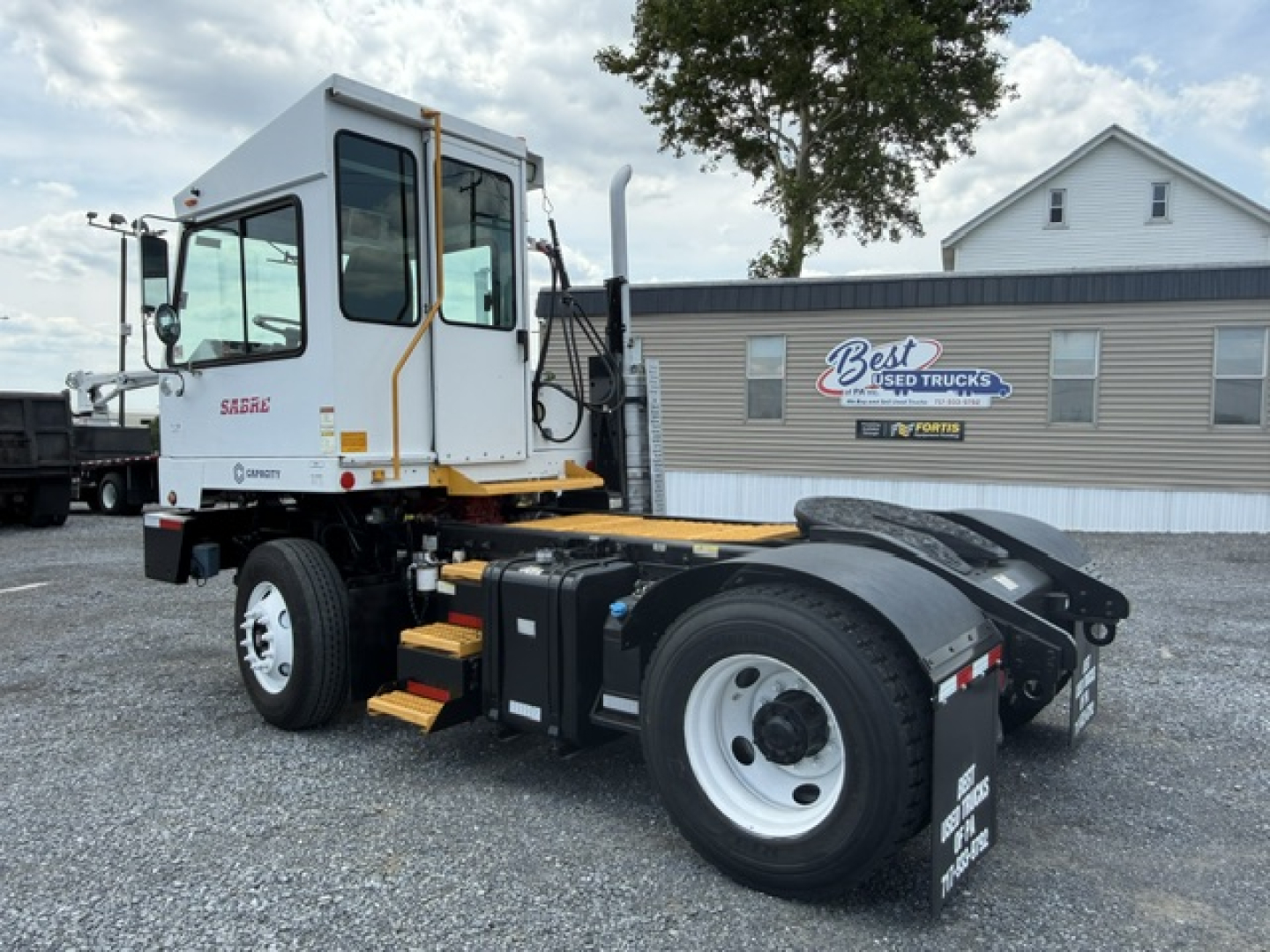 Truck chassis and cab showing Capacity Sabre DOT logo on door and wheel fender, with yard building in background.