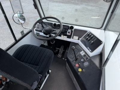 Bus/tractor cab interior showing steering wheel, dashboard with gauges, gear levers, and pedals.