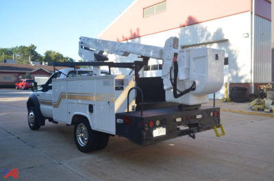 Truck with hydraulic boom lift mounted on chassis, rear view showing bucket, white utility body, and stabilizing outriggers.