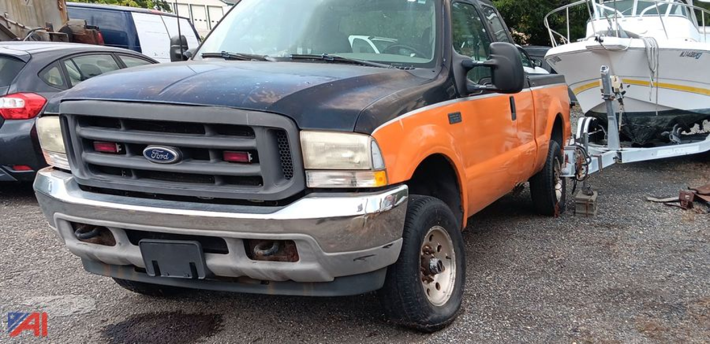 Front-left view of a Ford F-250 pickup with orange doors and black hood, showing grille with blue oval emblem and bumper; truck bed and other vehicles in background.