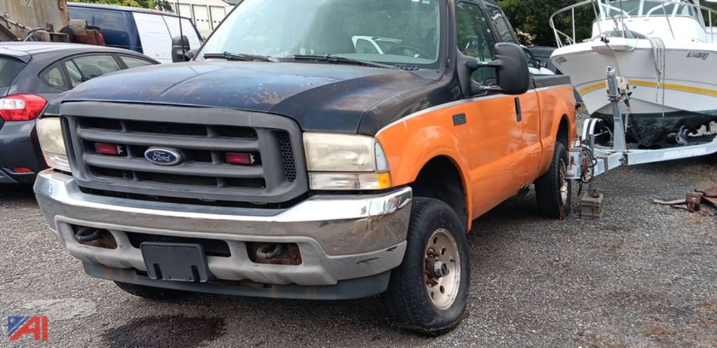 Front-left view of a Ford F-250 pickup with orange doors and black hood, showing grille with blue oval emblem and bumper; truck bed and other vehicles in background.