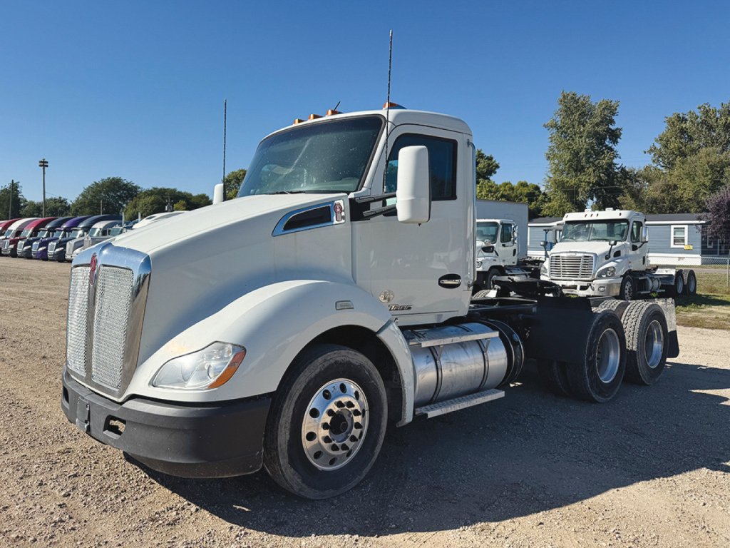 Kenworth T680 tractor unit in a parking lot with white cab, showing front grille, headlights, and dual rear axles. Visible text includes no legible markings on the cab.