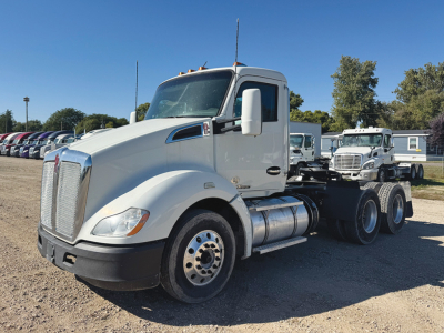 Kenworth T680 tractor unit in a parking lot with white cab, showing front grille, headlights, and dual rear axles. Visible text includes no legible markings on the cab.