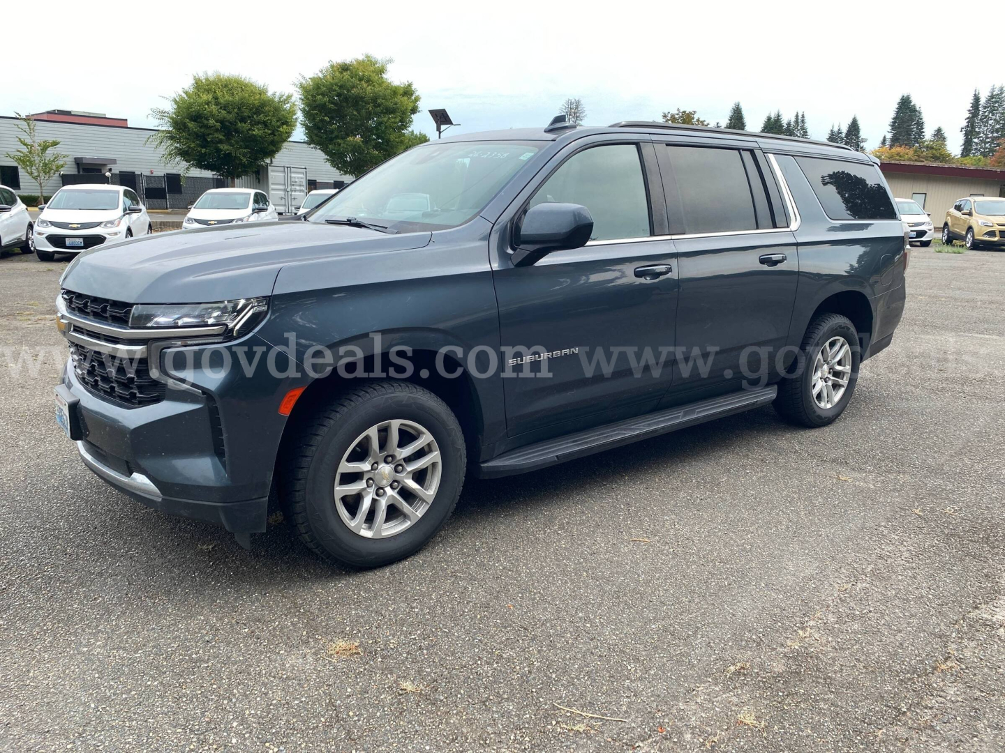 2021 Chevrolet Suburban SUV in a dealership lot showing front left side, chrome grille, LED headlights, side steps, tinted windows, and alloy wheels.