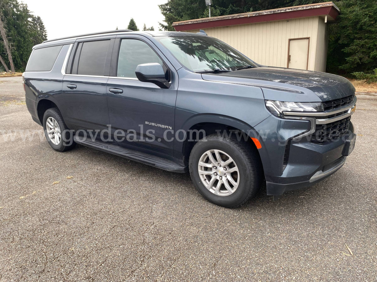 Chevrolet Suburban 2021 SUV in blue-gray with extended cargo area, side view showing front grille and headlights.