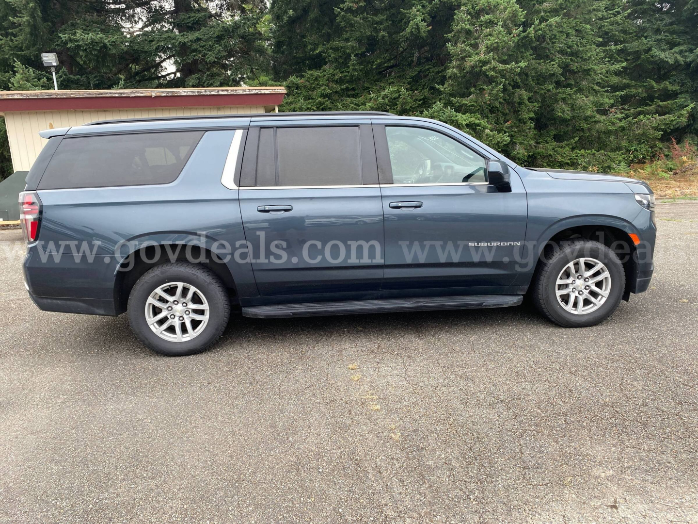 Chevrolet Suburban SUV side profile showing blue exterior, four doors, roof rails, and alloy wheels.