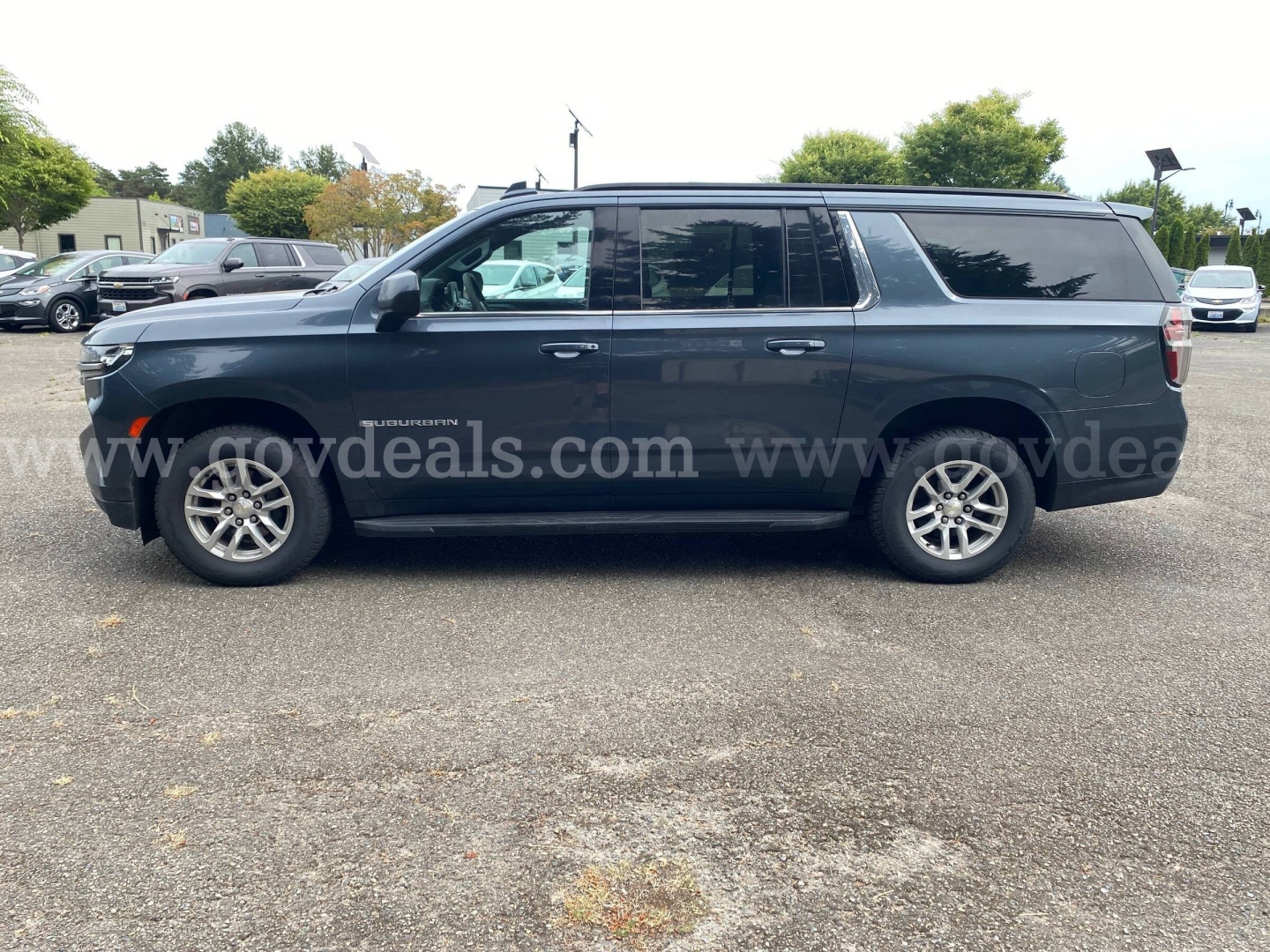 Chevrolet Suburban SUV in dark blue side profile view showing extended body with silver wheels and tinted windows.