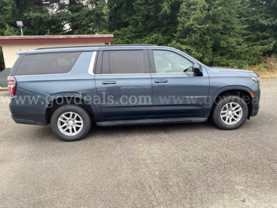 Chevrolet Suburban SUV side profile showing blue exterior, four doors, roof rails, and alloy wheels.