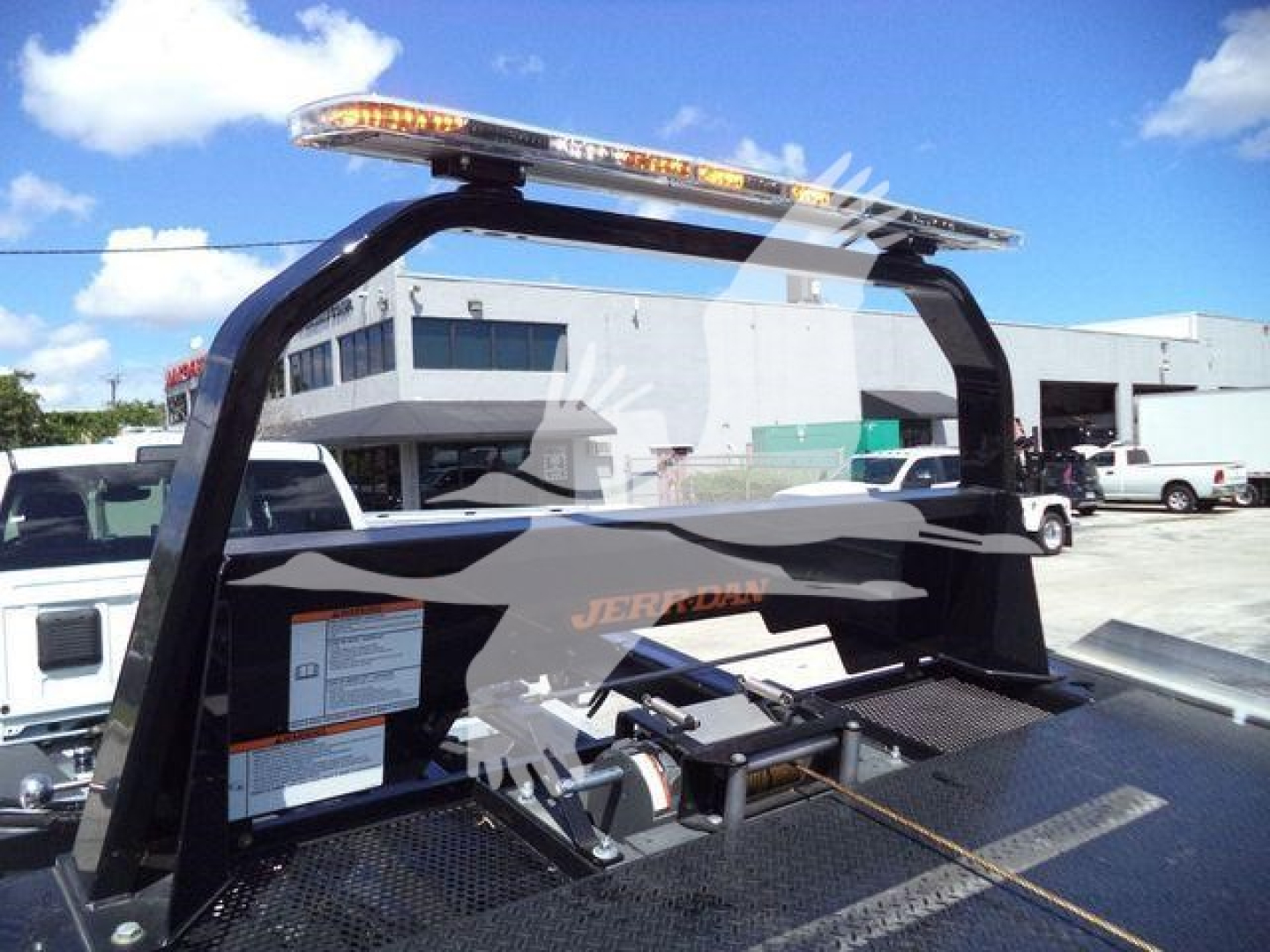 Ram 5500 rollback truck equipment with a dark roll cage and warning decals; platform with control box and tie-downs; orange light bar on top; background shows a service lot.