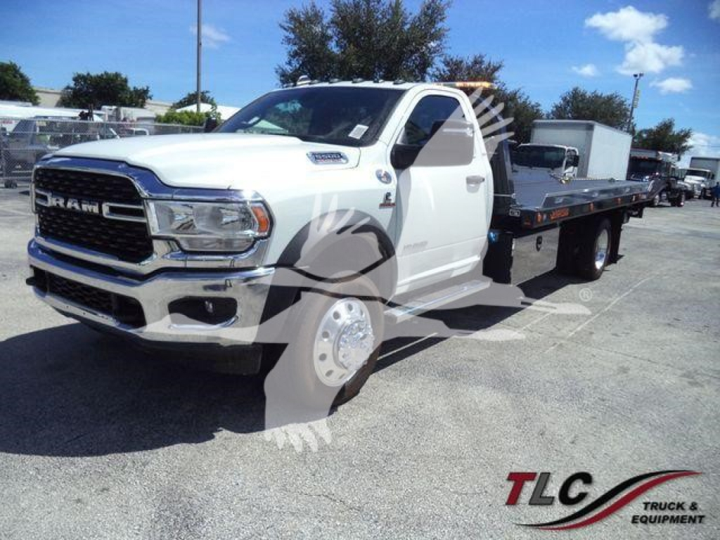 Ram 5500 rollback truck with flatbed in white, front grille and headlights visible, in a dealership lot.