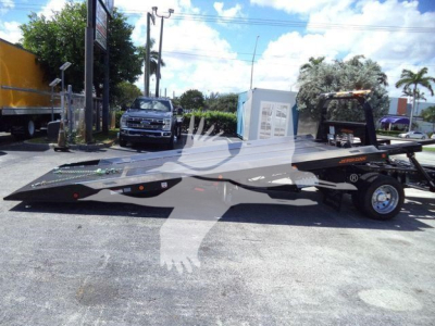 Ram 5500 rollback tow truck on trailer, side view with truck bed, black body, chrome wheel rims, dealership lot in background.