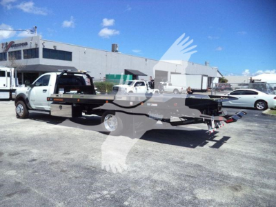 Ram 5500 rollback tow truck with flatbed and hitch, side view showing white cab and black flatbed.