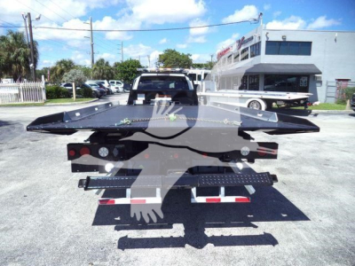 Ram 5500 rollback tow truck bed with flatbed and winch mounted, rear view in dealership lot.