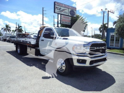 Ram 5500 SLT flatbed tow truck in dealership lot, front grill with RAM badge, white cab, long flatbed, dealership signs in background.
